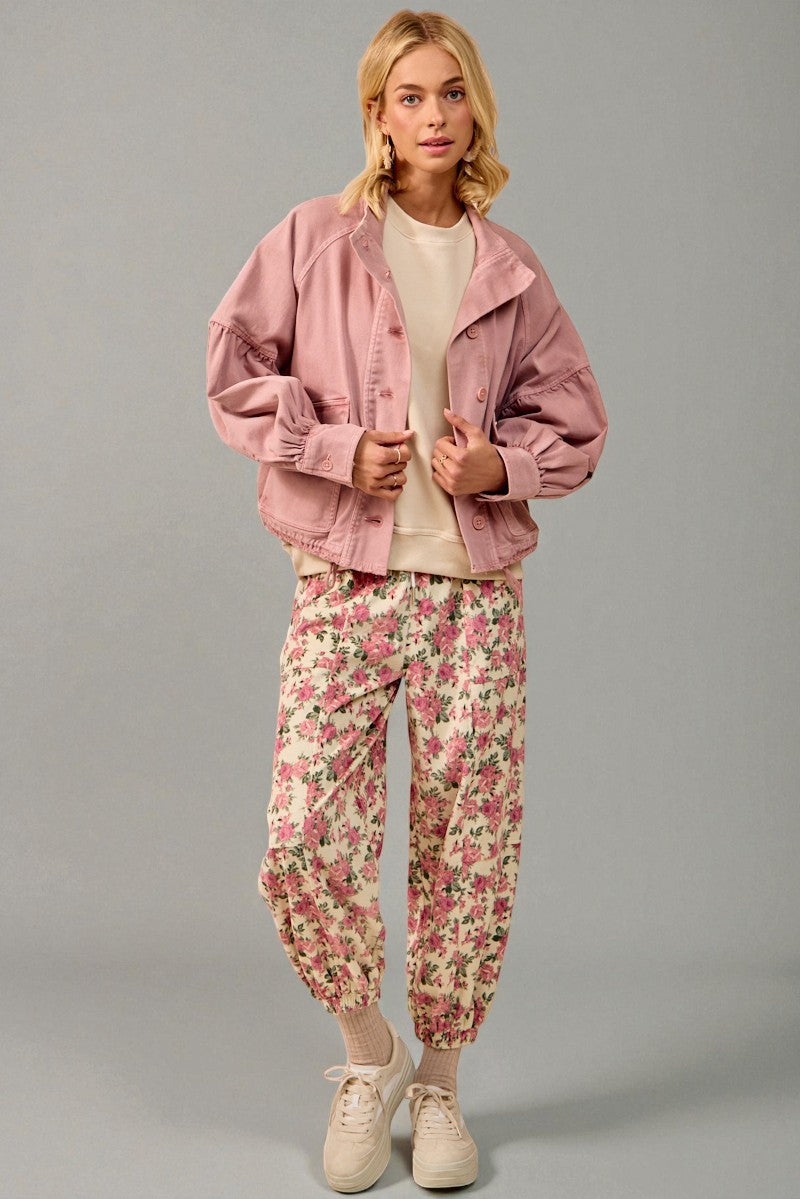 Woman wearing a pink jacket and floral pants on a gray background