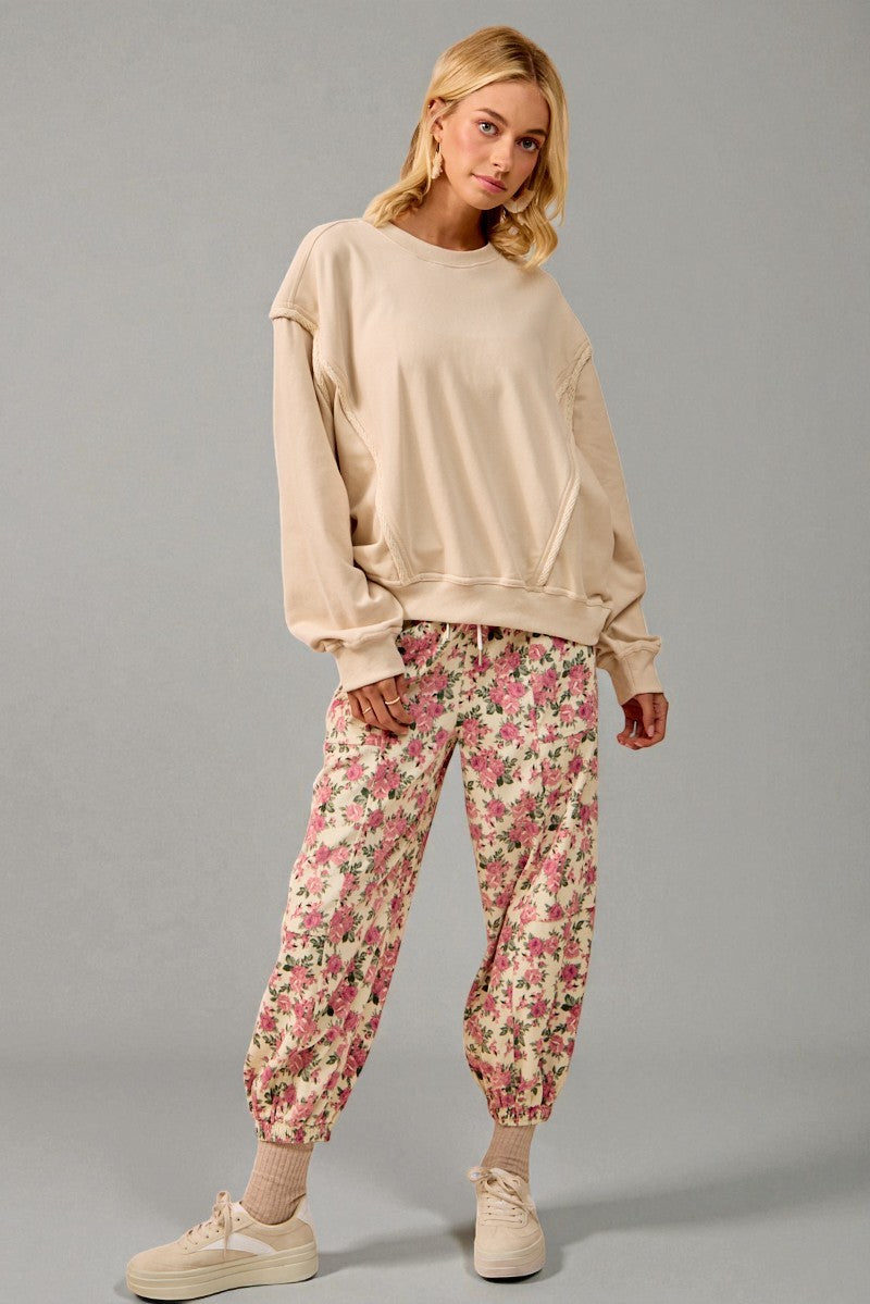 Woman wearing a beige sweatshirt and floral pants on a gray background