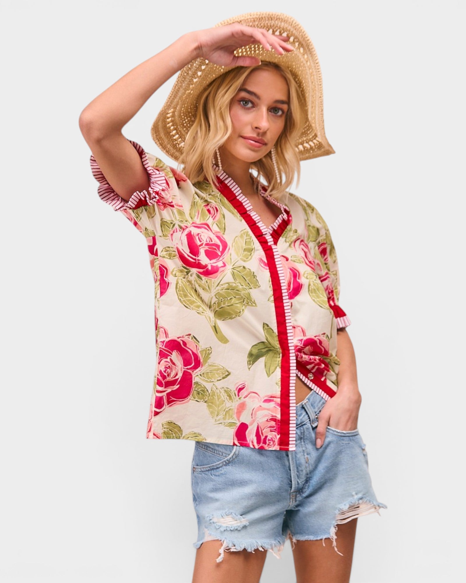 Woman wearing a floral kimono-style top and denim shorts with a straw hat on a white background