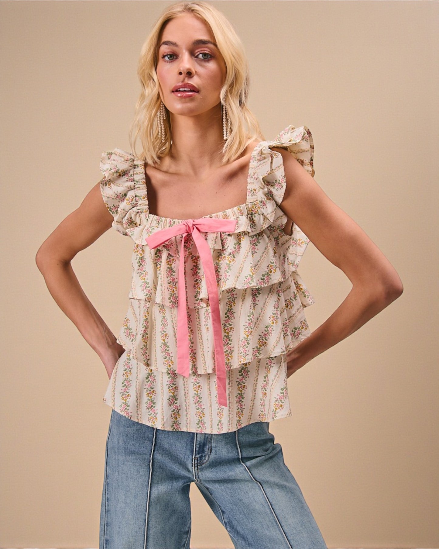 Woman wearing a floral blouse with a pink ribbon and jeans on a beige background