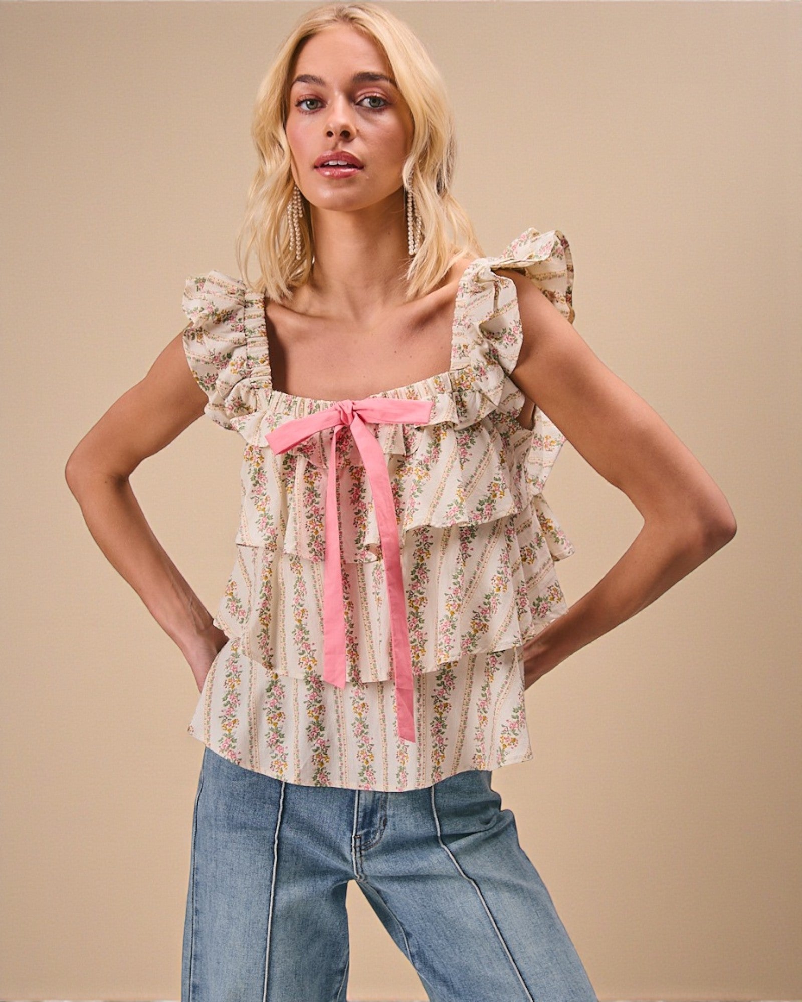 Woman wearing a floral blouse with a pink ribbon and jeans on a beige background
