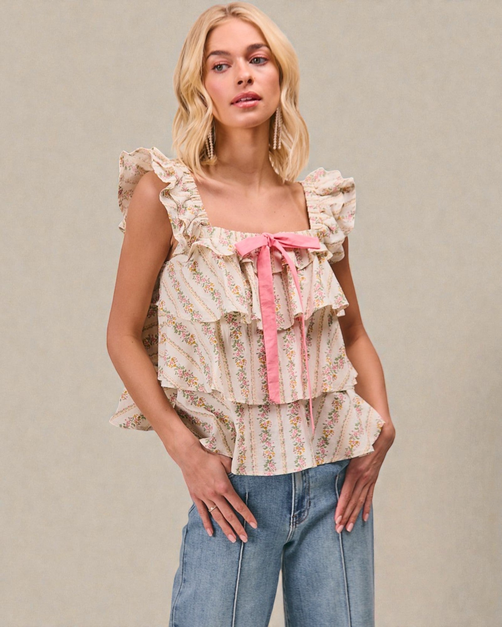 Woman wearing a floral top with ruffles and a pink ribbon, standing against a plain background