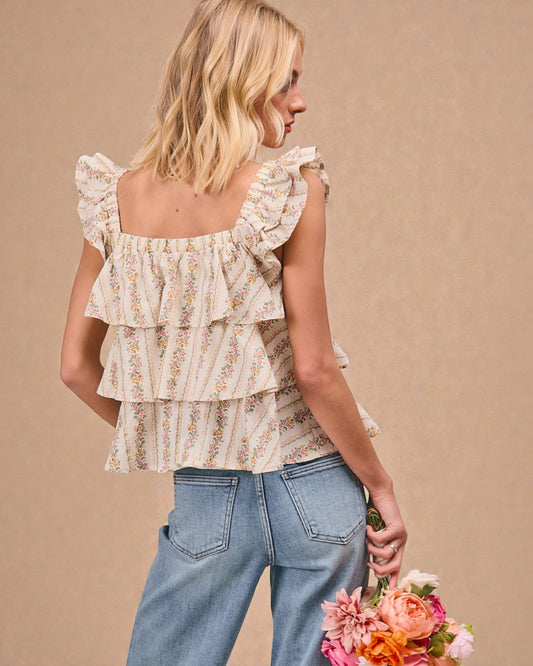 Woman wearing a floral tiered blouse and jeans, holding flowers against a beige background