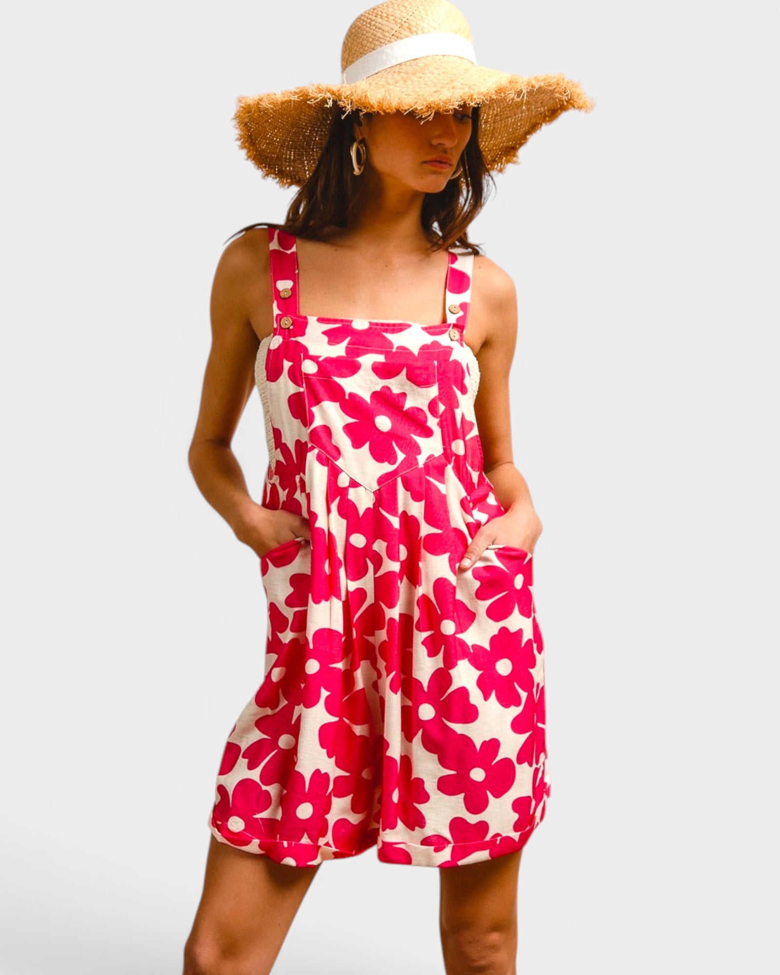 Woman wearing a pink floral dress and straw hat on a plain background