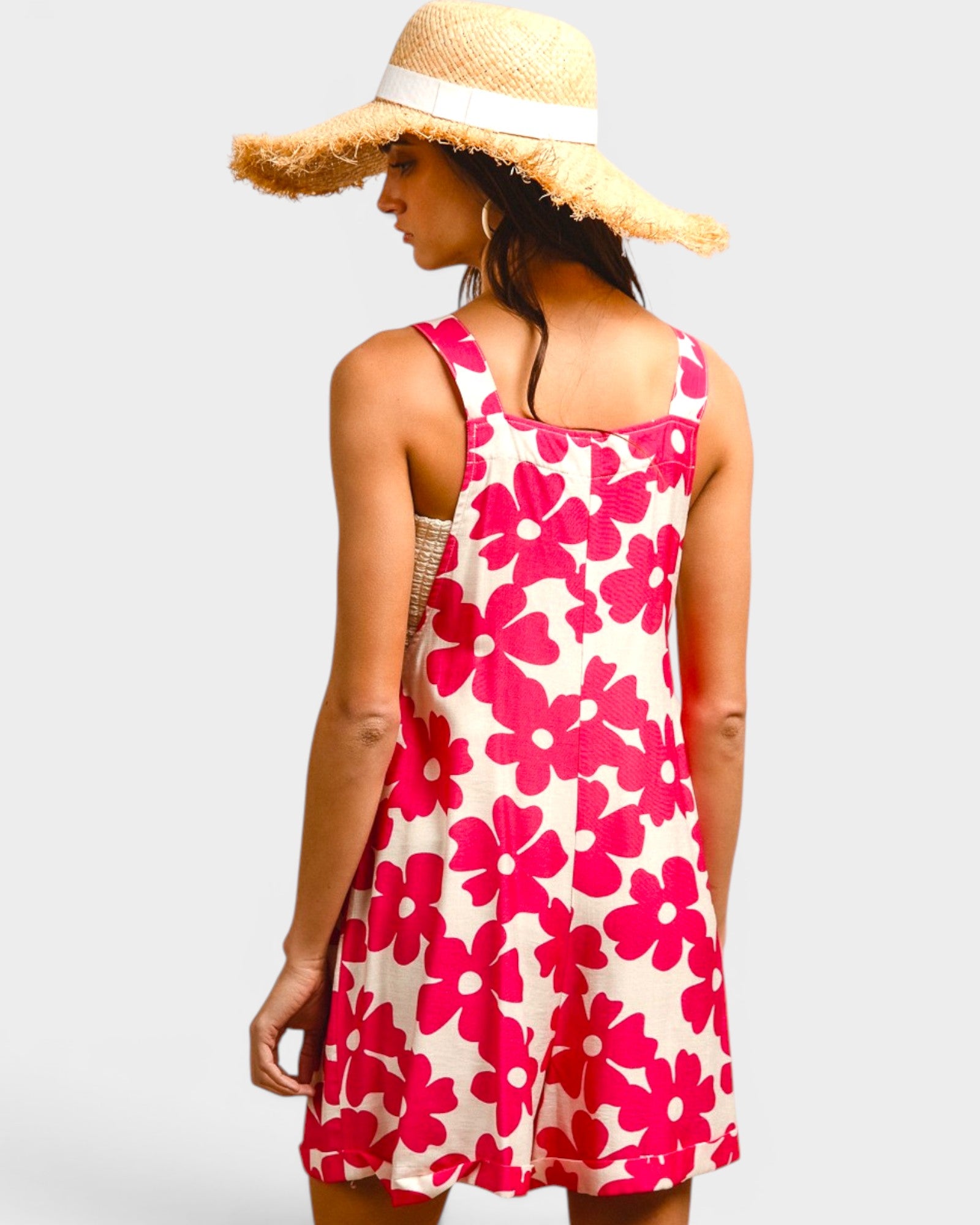 Woman wearing a pink floral dress and straw hat on a light gray background
