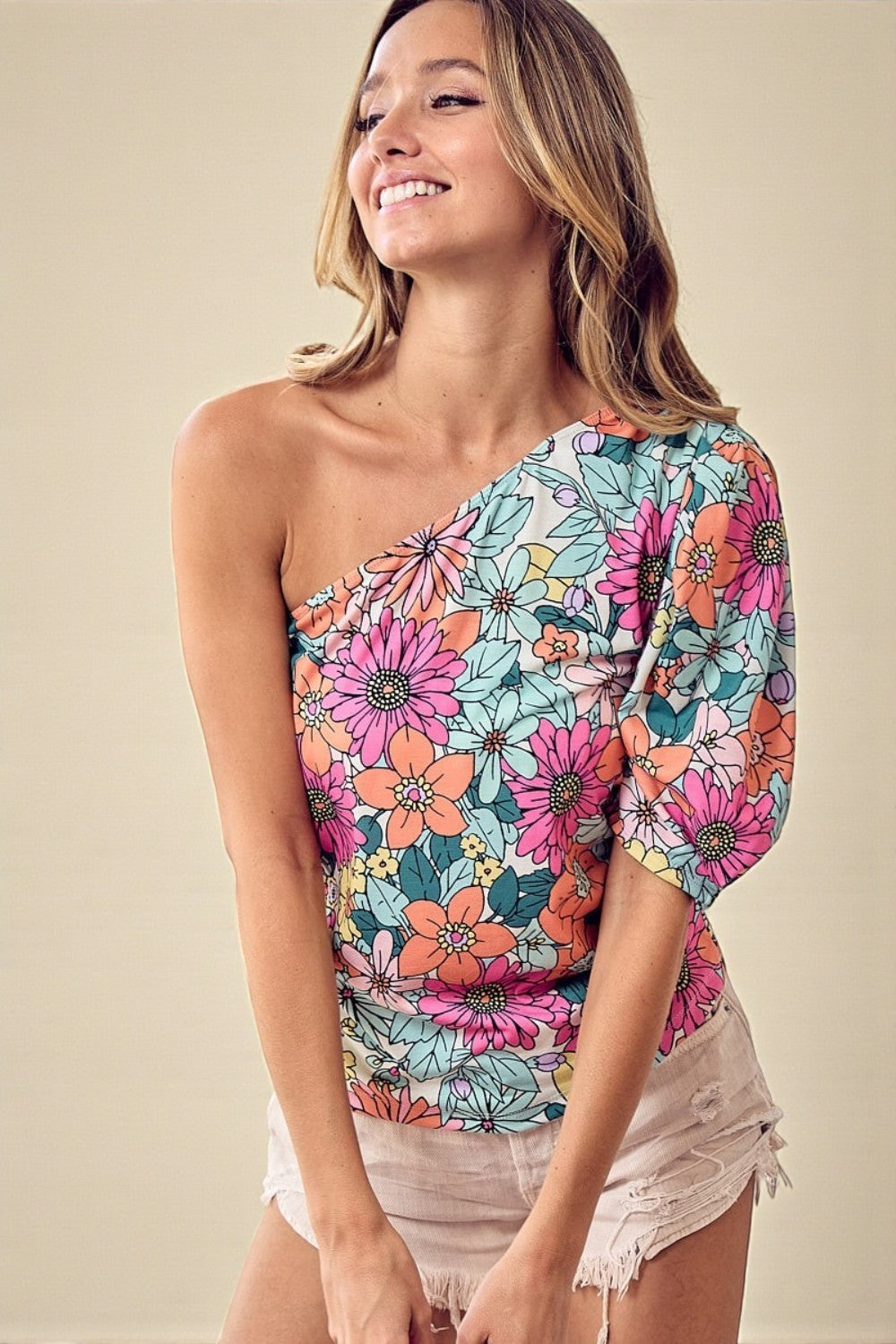 Woman wearing a colorful floral one-shoulder top against a beige background