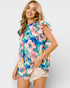 Woman wearing a colorful floral top and white shorts on a plain background