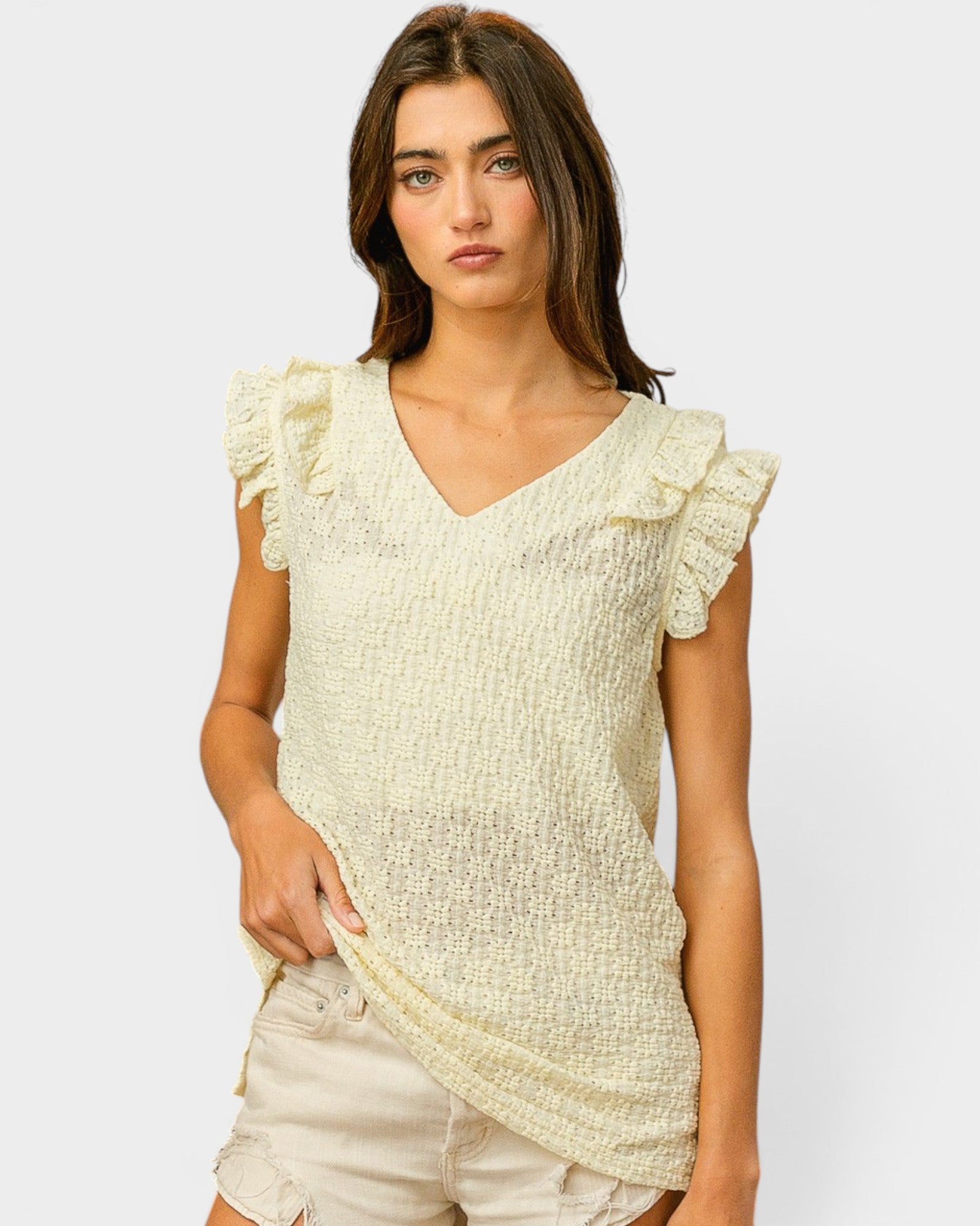 Woman wearing a light-colored top with ruffled sleeves on a plain background