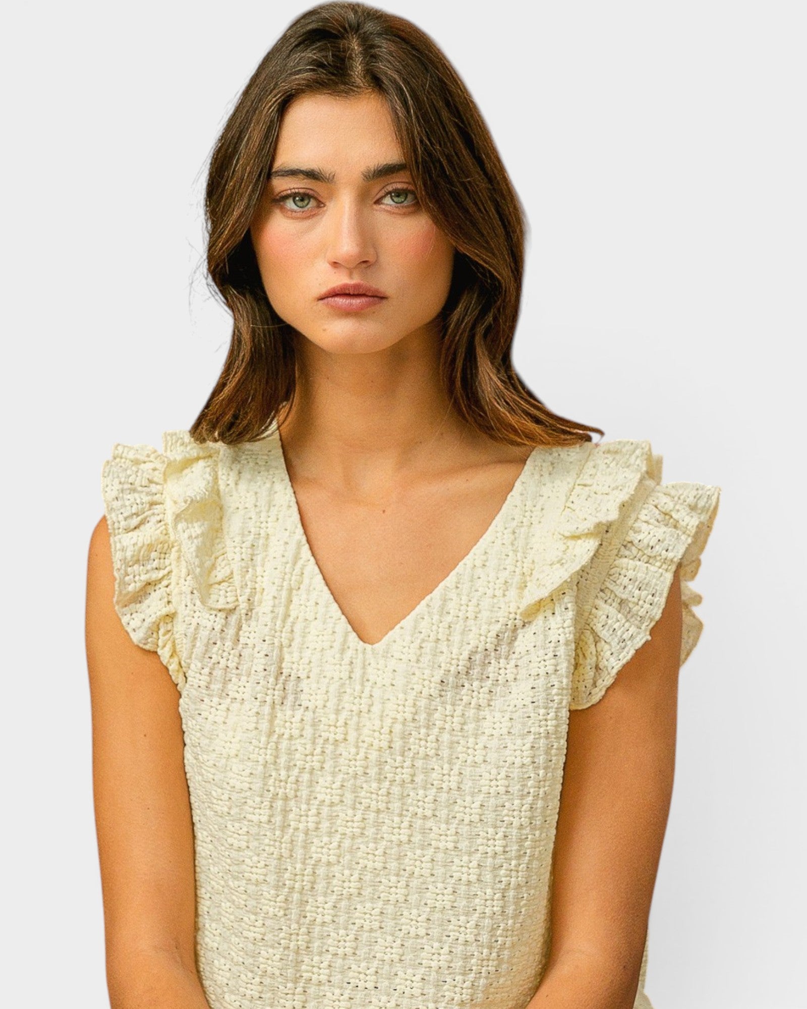 Woman wearing a light-colored top with ruffled sleeves on a plain background