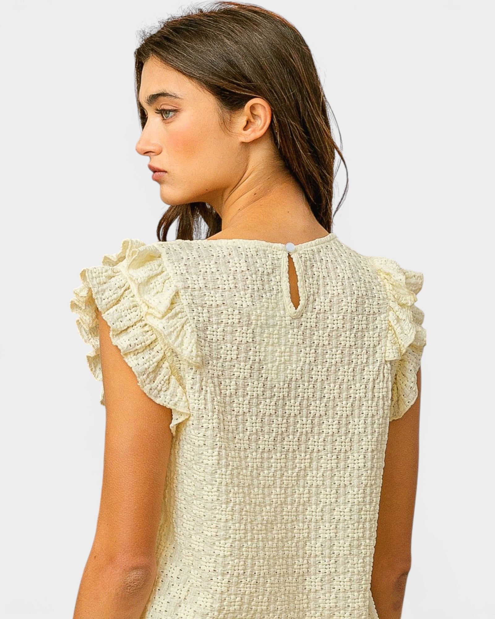 Woman wearing a light-colored top with ruffled sleeves on a plain background