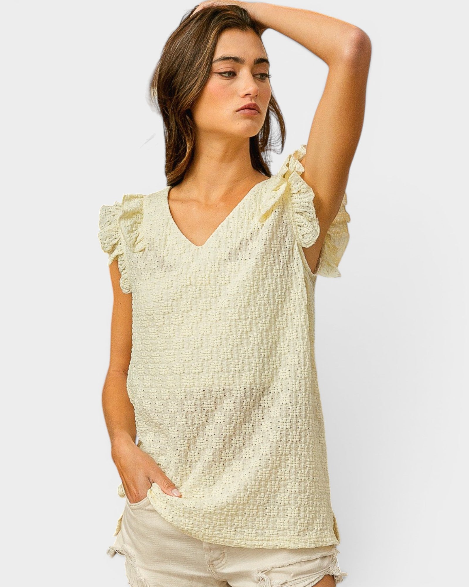 Woman wearing a light-colored textured top with ruffled sleeves on a plain background