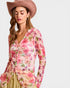 Woman wearing a floral dress and wide-brimmed hat on a plain background