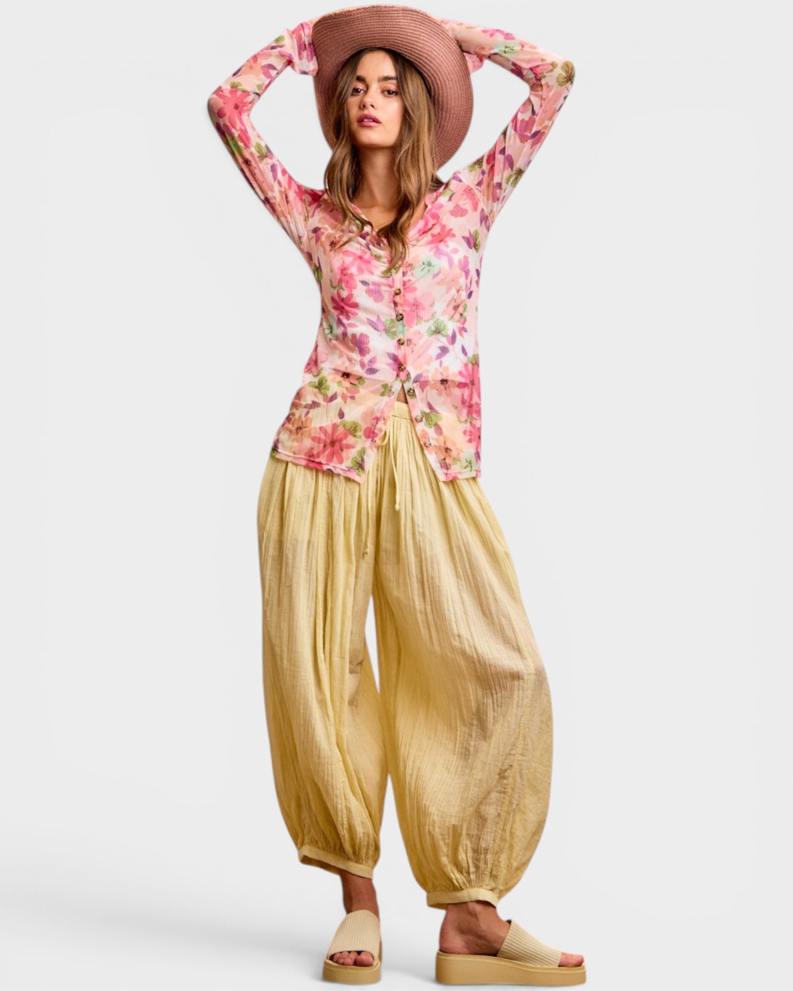 Woman wearing a floral top and wide-leg pants with a hat on a white background