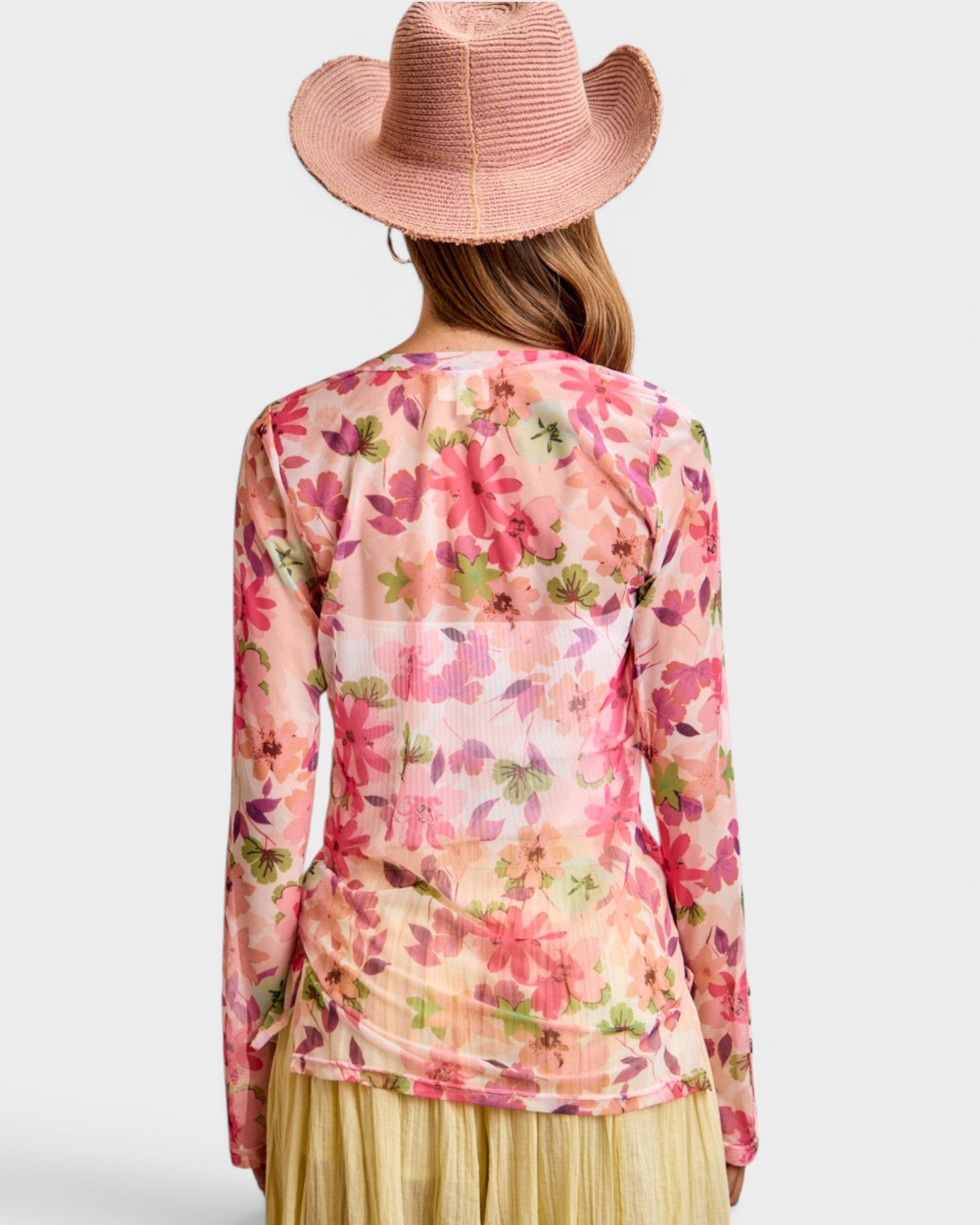 Person wearing a floral long-sleeve top and pink hat on a white background