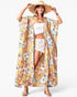 A woman modeling a long, open-front kimono-style cover-up with a yellow base and a multicolor floral print, worn over a white crop top and light denim shorts, with a wide-brim straw hat and sandals.