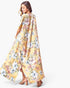 A woman modeling a long, flowing yellow floral dress or caftan with a side slit, shown from a three-quarter back angle against a plain light gray studio background.