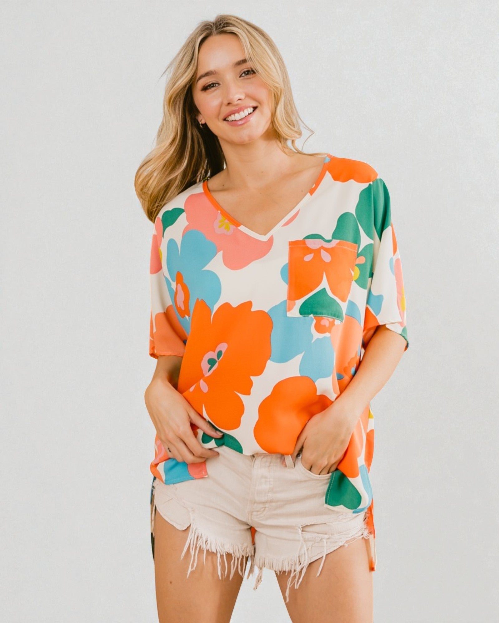 Woman wearing a colorful floral shirt and shorts on a plain background
