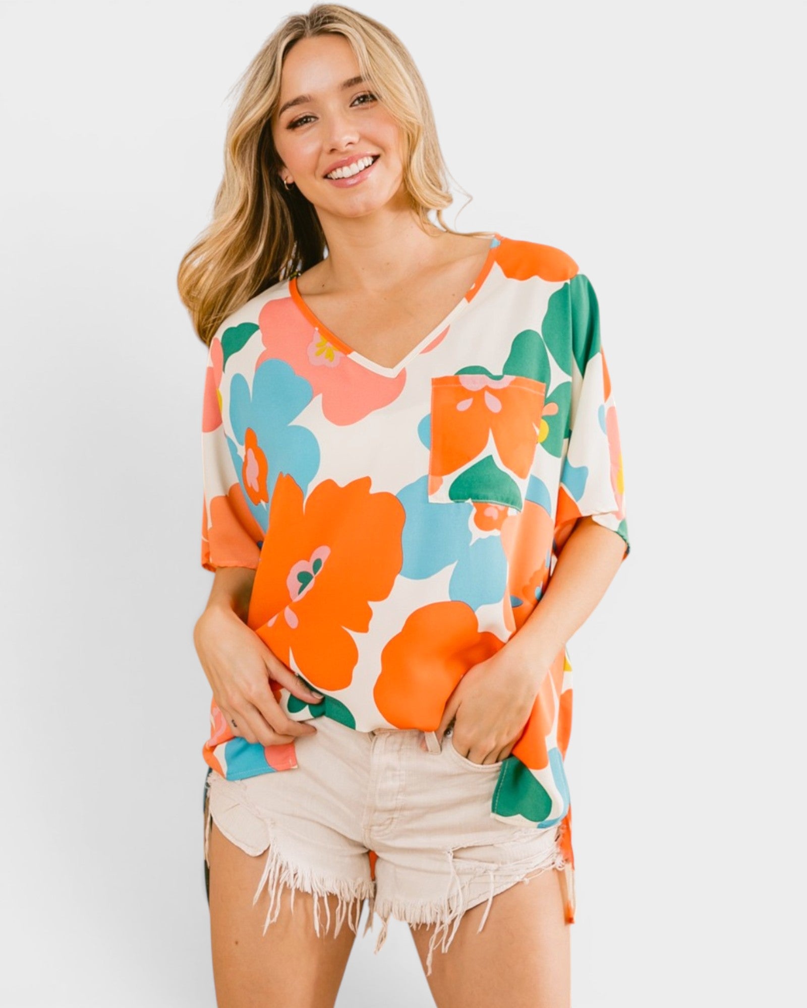 Woman wearing a colorful floral shirt and shorts on a plain background