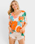 Woman wearing a colorful floral shirt and shorts on a plain background