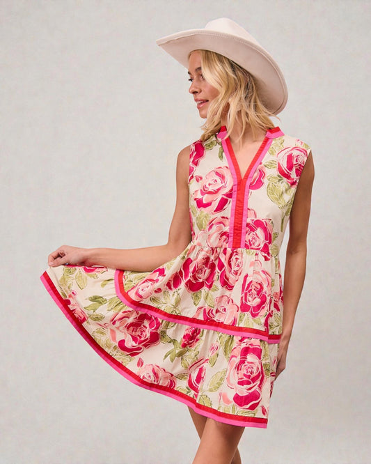 Woman wearing a floral dress with pink roses and a white hat on a plain background