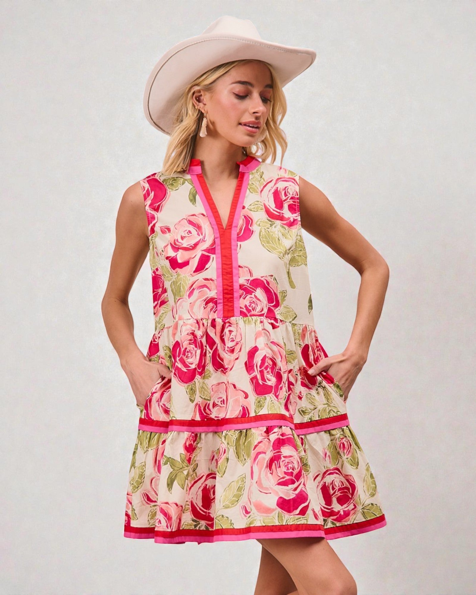 Woman wearing a floral dress with pink roses and a white hat on a light gray background