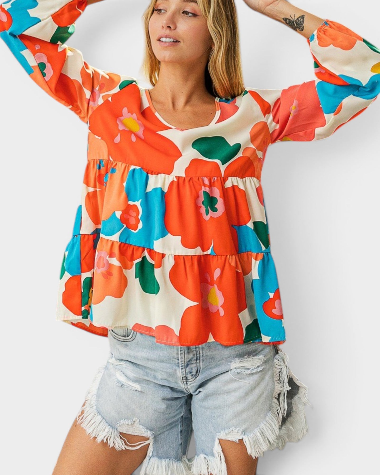 Woman wearing a colorful floral blouse with long sleeves and denim shorts on a white background