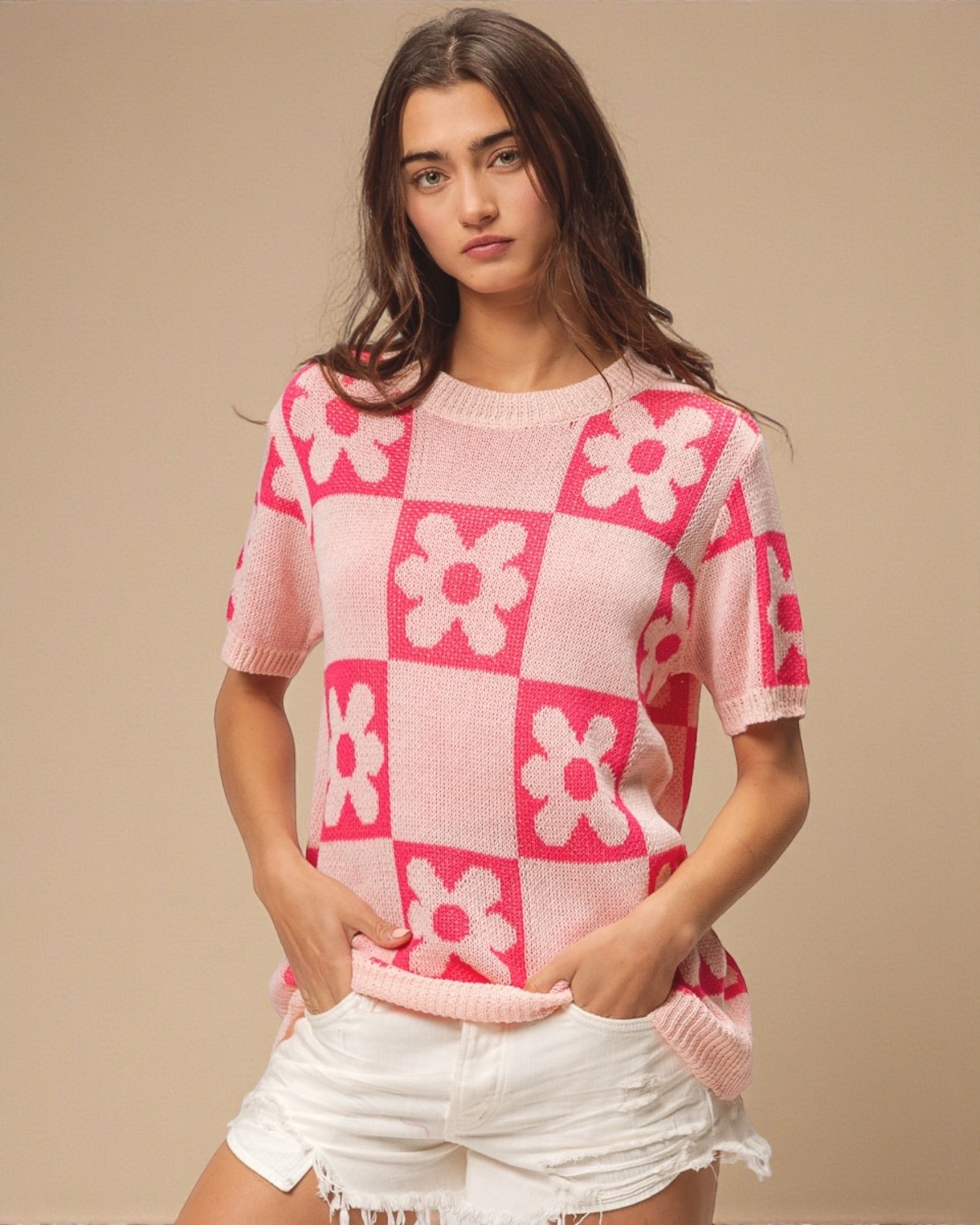 Woman wearing a pink and white checkered sweater with floral patterns on a beige background
