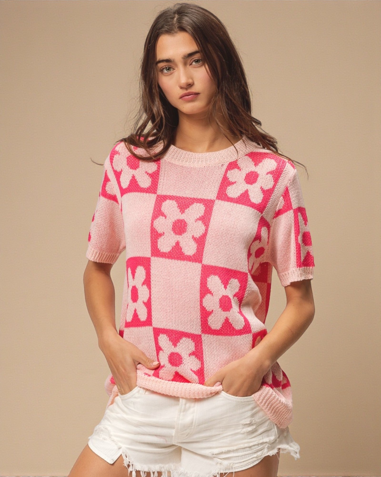 Woman wearing a pink and white checkered sweater with floral patterns on a beige background