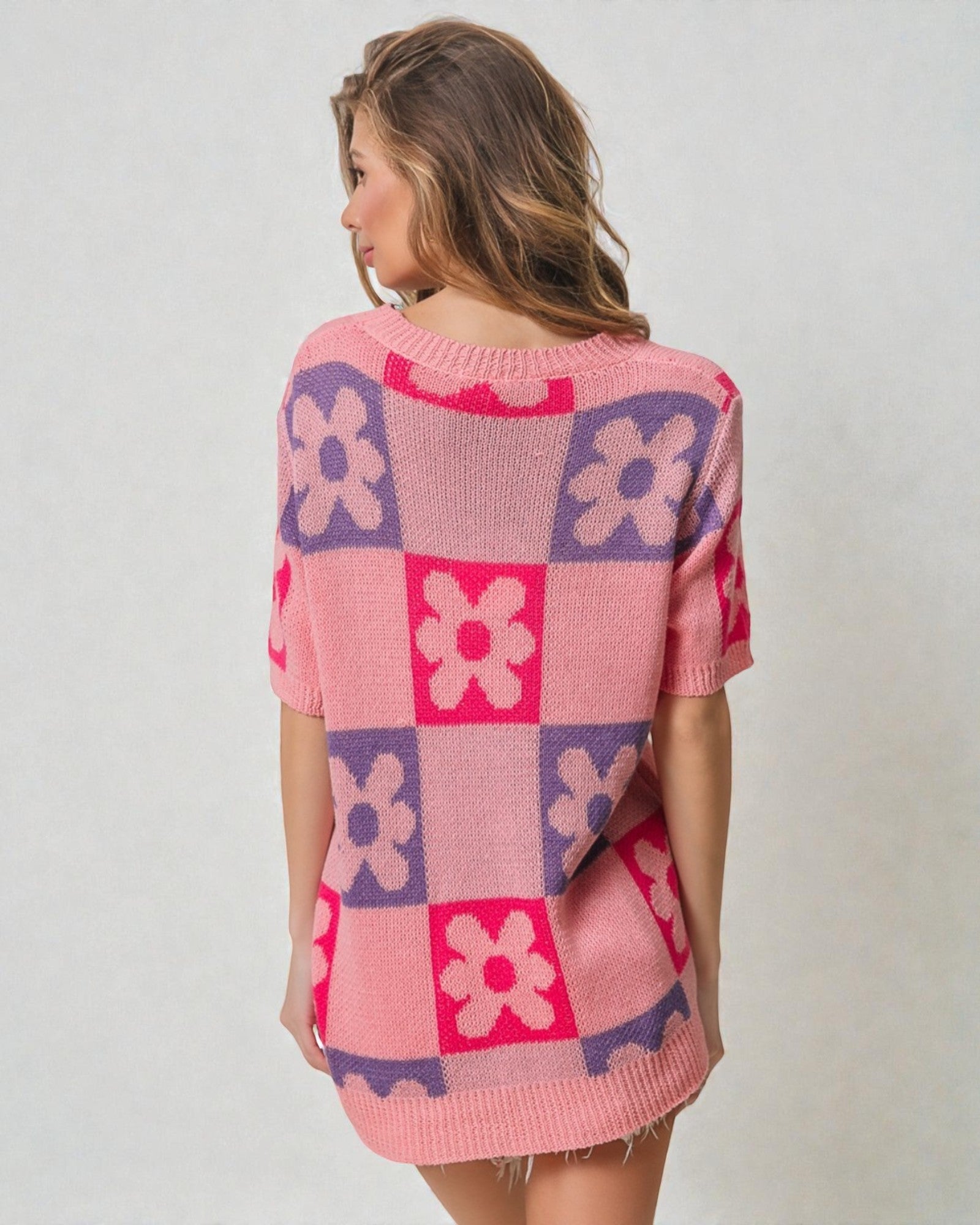 Woman wearing a pink and purple checkered sweater with floral patterns on a plain background