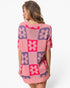 A woman wearing a pink knit sweater with a purple and pink checkerboard floral pattern, shown from the back against a light gray studio background.
