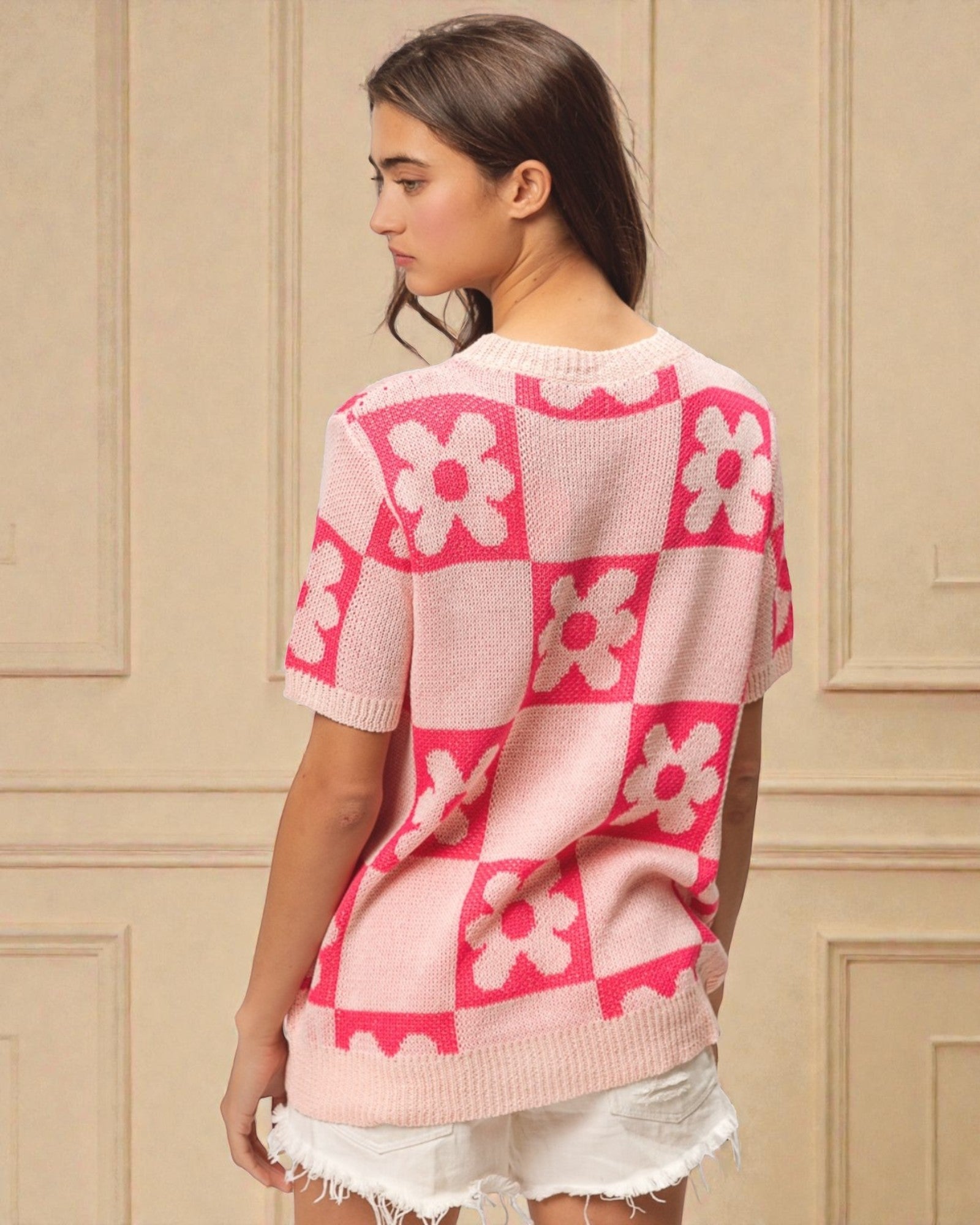 Woman wearing a pink floral patterned sweater against a beige wall.