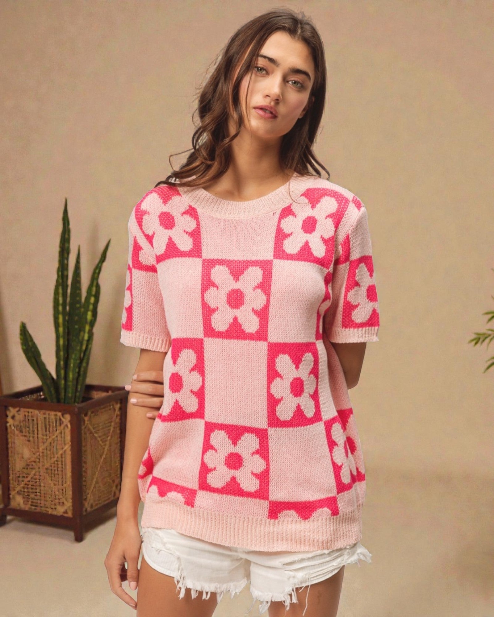 Woman wearing a pink and white checkered sweater with floral patterns against a beige background.