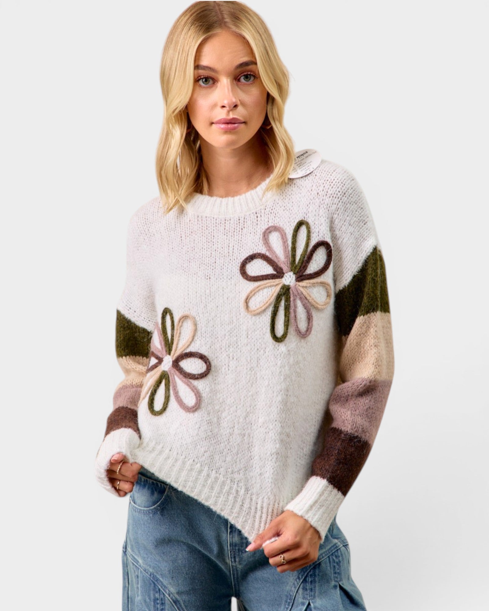Woman wearing a white sweater with flower patterns on a plain background