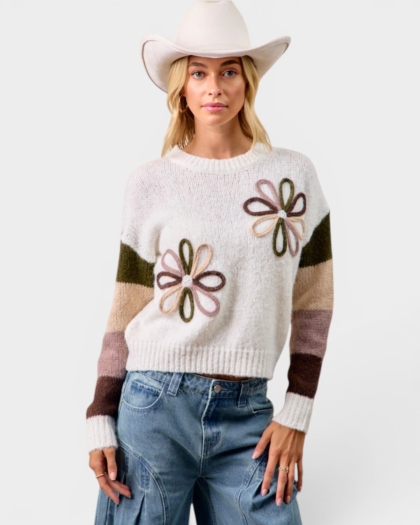 Woman wearing a white sweater with flower patterns, blue jeans, and a white cowboy hat on a white background