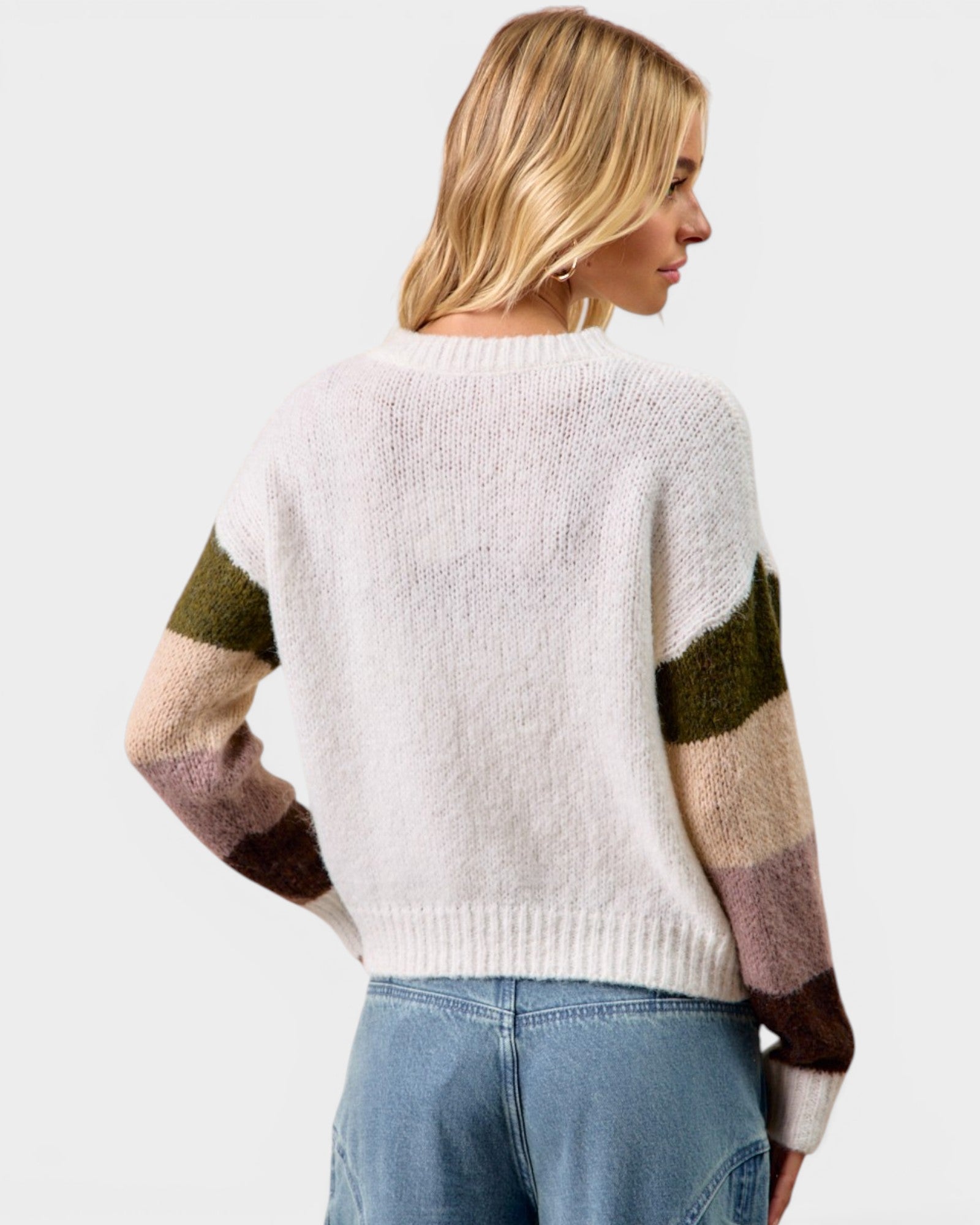 Woman wearing a white sweater with color-blocked sleeves on a light gray background