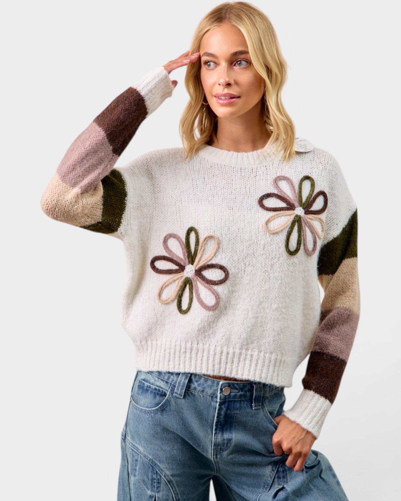 Woman wearing a white sweater with flower patterns and colorful sleeves on a light gray background