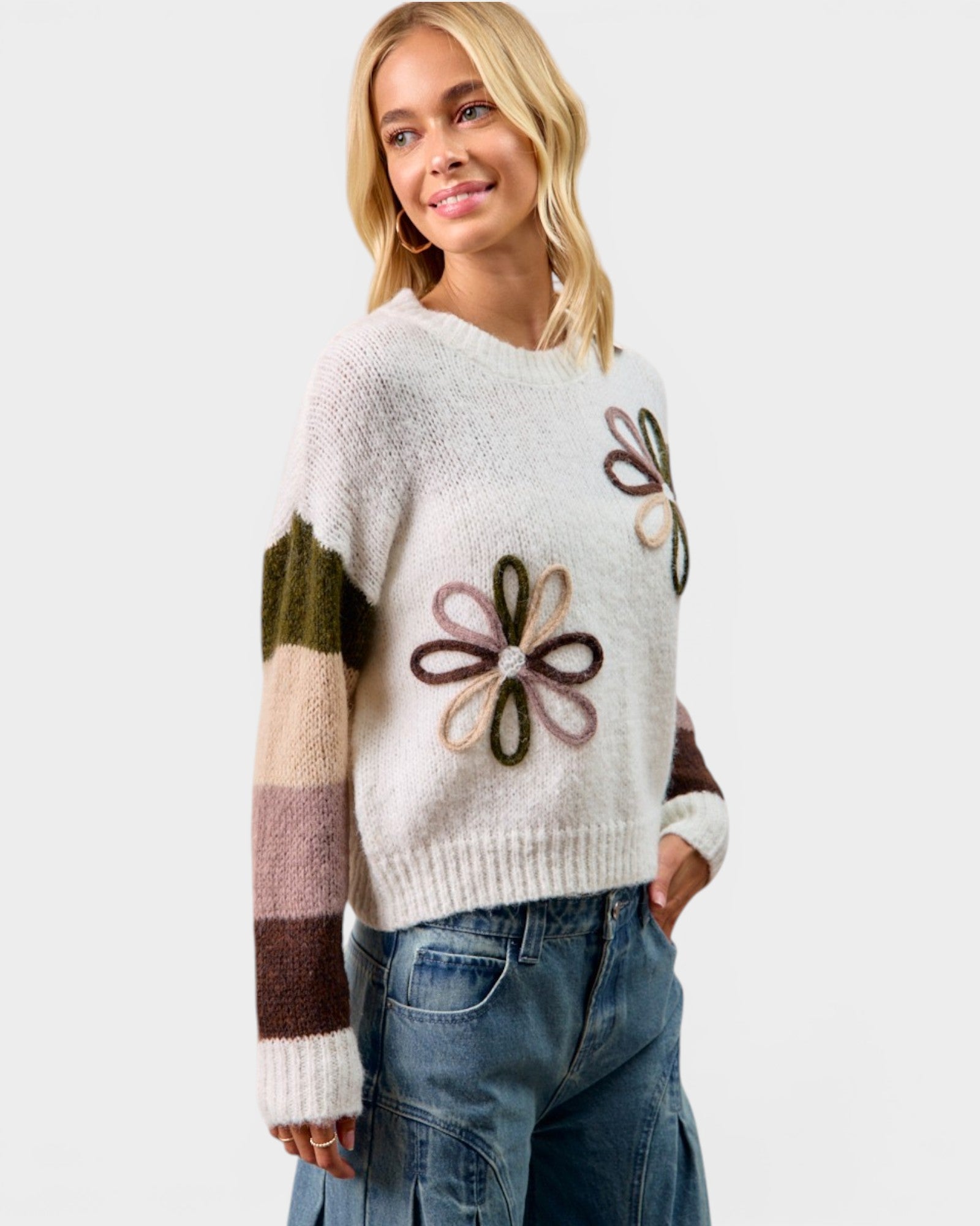 Woman wearing a white sweater with floral patterns on a plain background