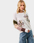 Woman wearing a sweater with floral designs on a plain background