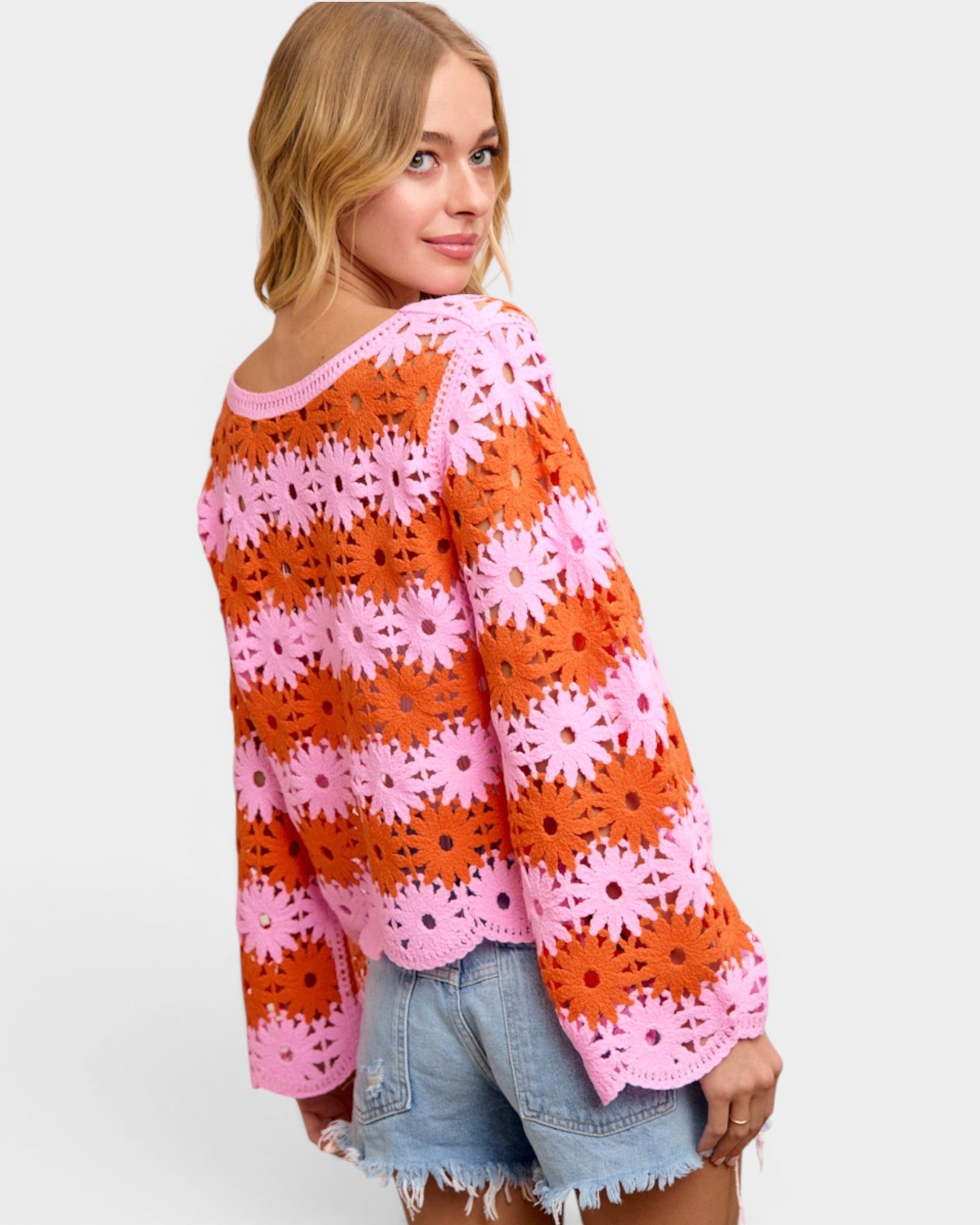 Woman wearing a colorful crochet sweater with pink and orange patterns on a white background