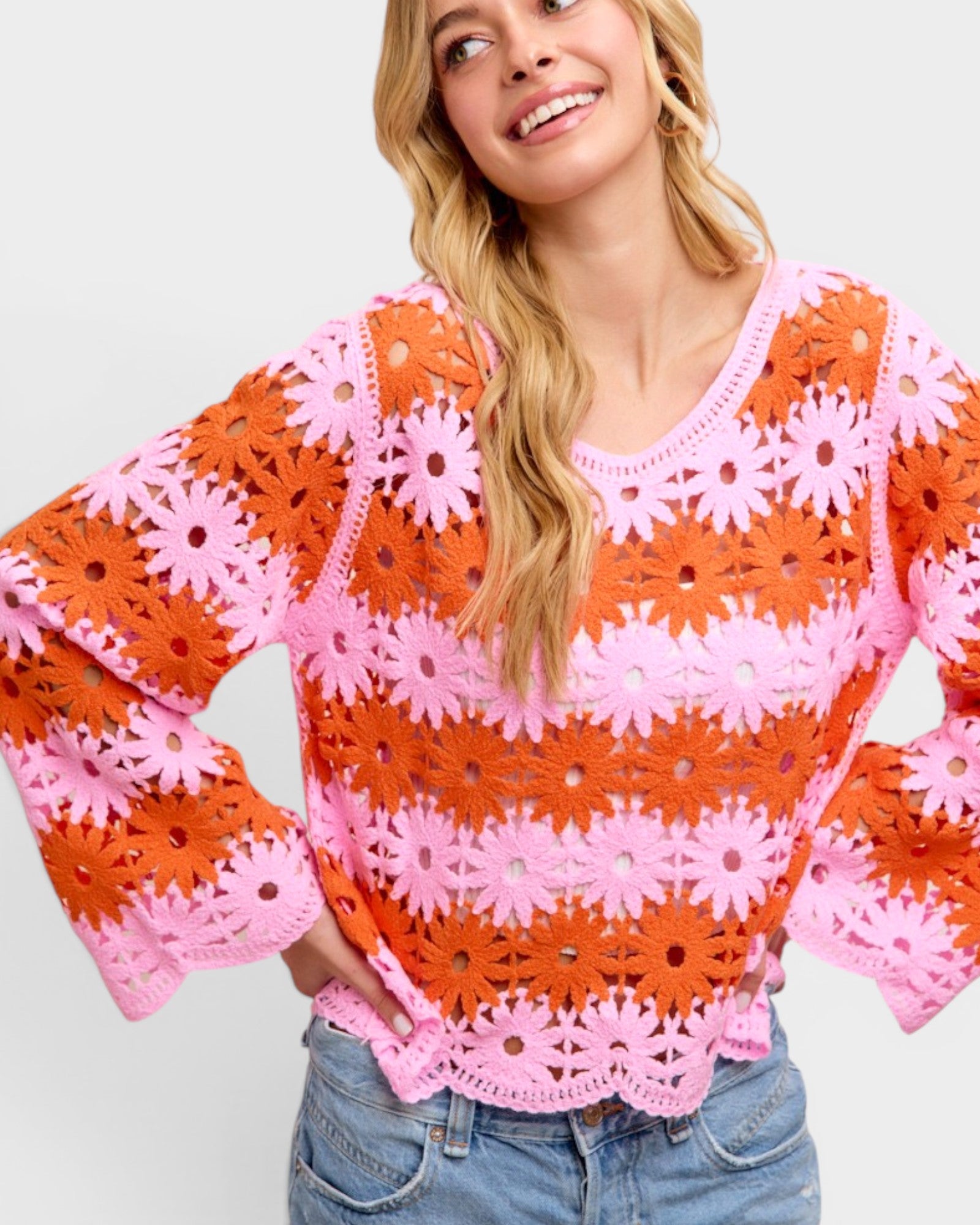 Woman wearing a colorful crochet sweater with pink and orange flowers on a light gray background