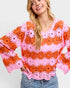 Woman wearing a colorful crochet sweater with pink and orange flowers on a light gray background
