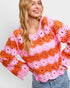 Woman wearing a colorful crochet sweater with pink and orange flowers on a light gray background