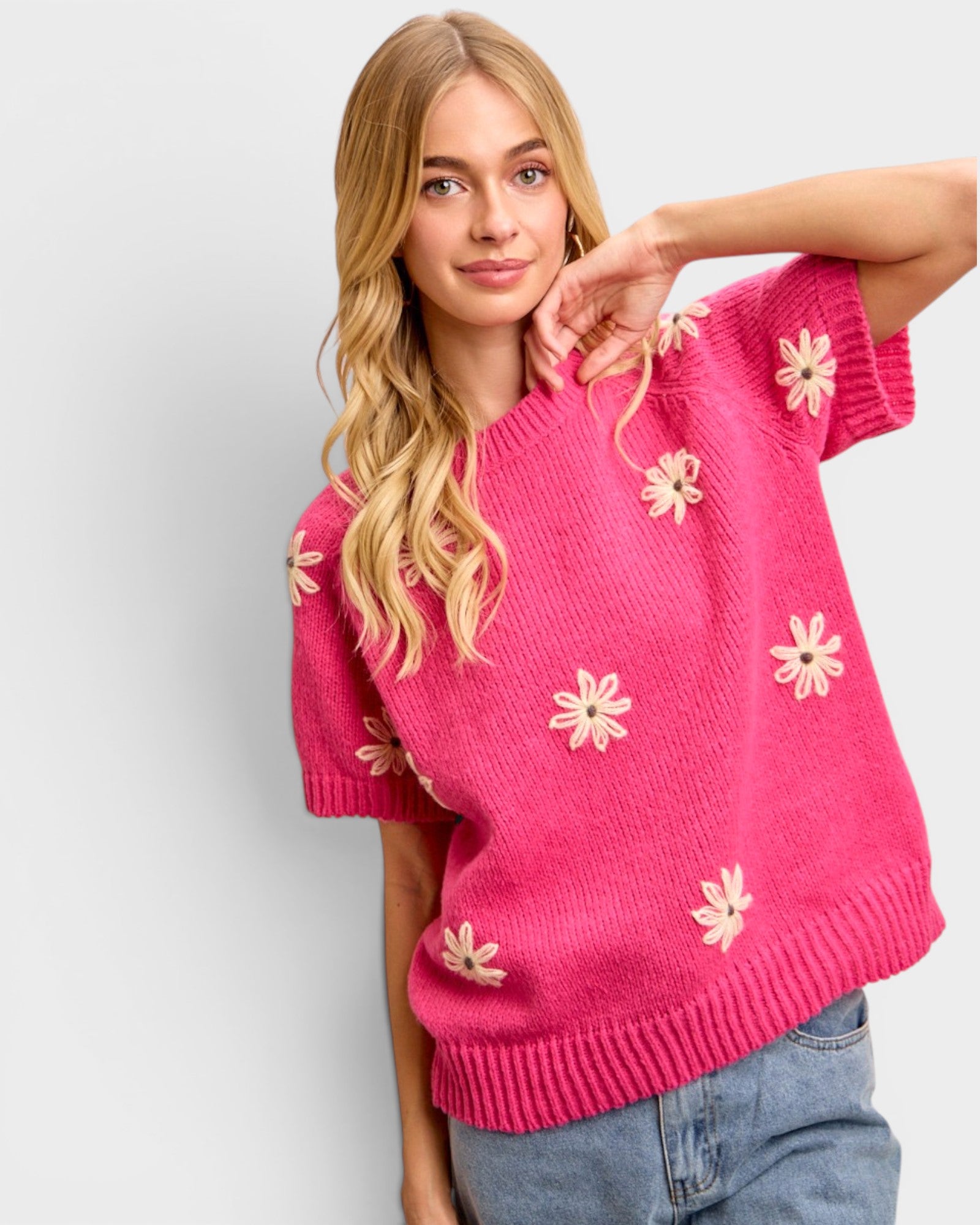 Woman wearing a pink sweater with floral patterns on a plain background