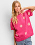 Woman wearing a pink sweater with floral patterns on a plain background