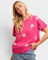 Woman wearing a pink sweater with floral patterns on a plain background
