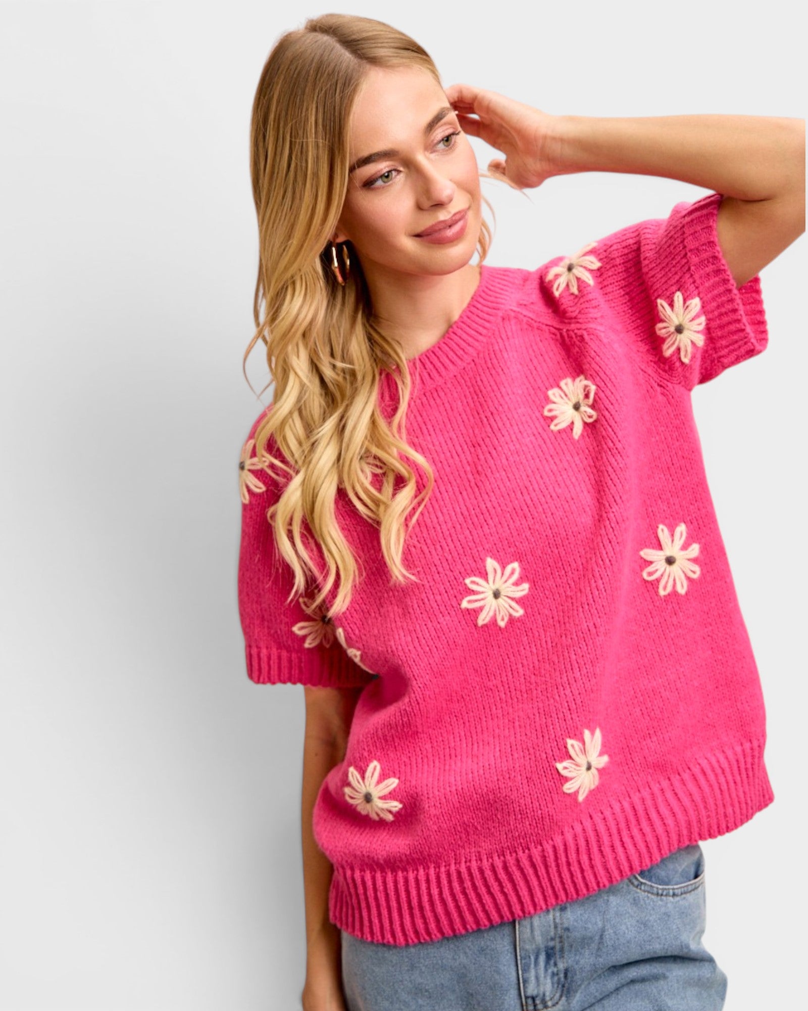 Woman wearing a pink sweater with floral patterns against a plain background