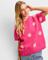 Woman wearing a pink sweater with floral patterns against a plain background