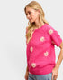 Woman wearing a pink sweater with white floral patterns on a plain background
