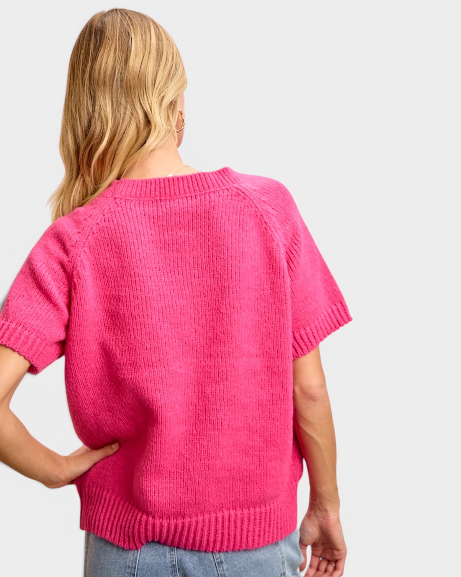 Person wearing a bright pink knitted sweater on a plain background