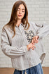 Woman wearing a striped shirt with a floral design in front of a white brick wall.